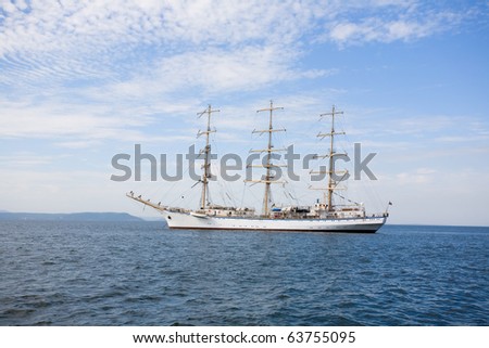 Big sailing ship is at anchor in port. At the stern of the vessel flag of Russia.