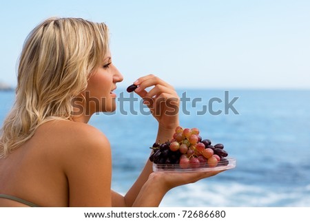 Attractive girl eating grapes at the beach by the sea.