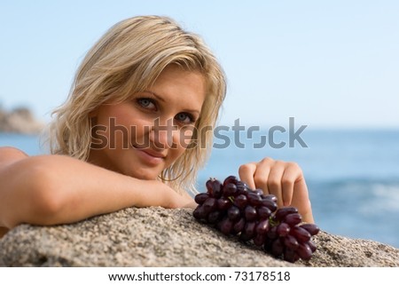 Beautiful girl and grapes at the beach by the sea.