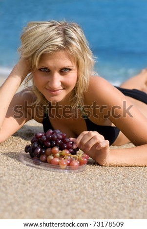 Beautiful girl with grapes on the beach by the sea.