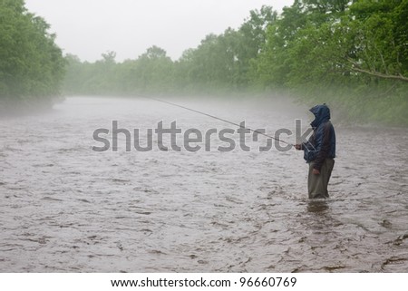 Fisherman catches a salmon river. Fog. Is rain. Morning.