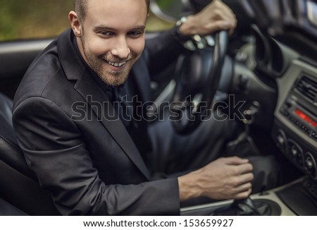 Elegant young happy man in convertible car outdoor. Close-up face photo.