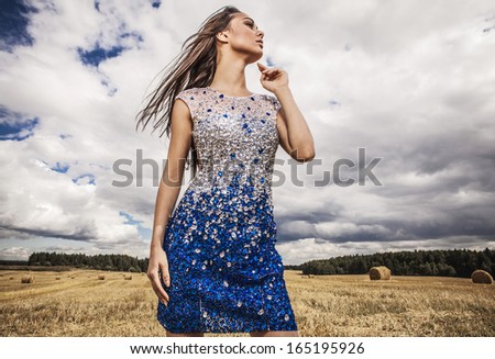 Young sensual & beauty woman in a fashionable white-blue dress pose on field.