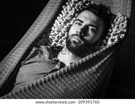 Portrait of young handsome serious man in a hammock. Black-white close-up photo.