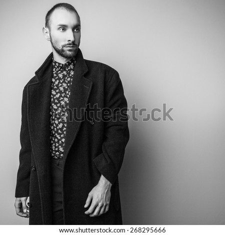 Elegant young handsome man in long wool coat. Black-white studio fashion portrait.