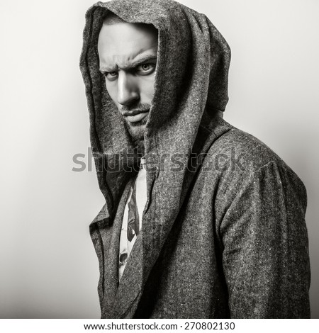 Studio portrait of young handsome man in casual cape with a hood. Close-up sepia photo.