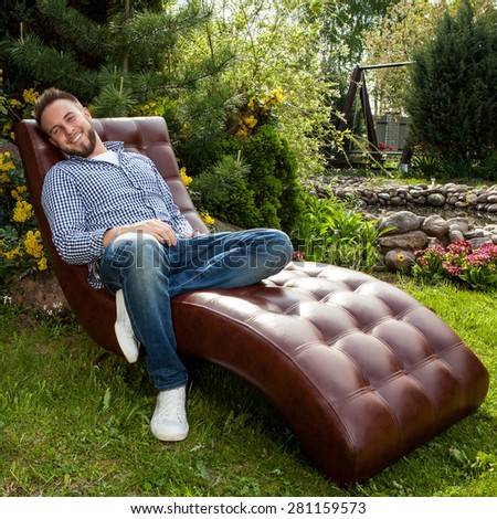 Young handsome man in casual clothes sit in luxury sofa in summer garden.