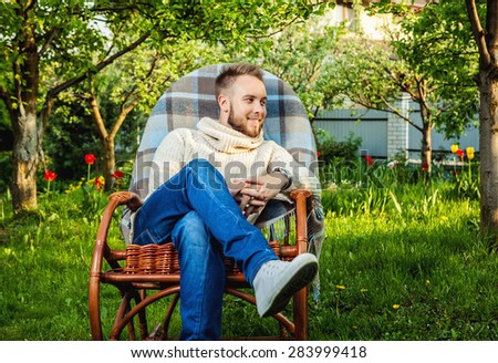 Handsome man relax in rocking-chair with plaid in a summer garden.