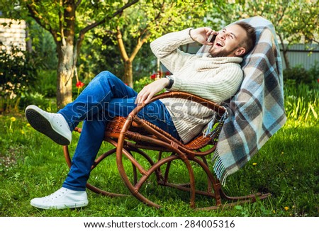 Handsome man relax in rocking-chair with plaid & phone in a summer garden.