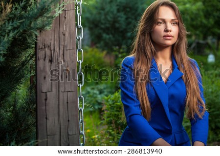 Attractive young woman in official blue suit poses in summer garden.