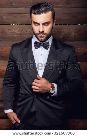 Portrait of young beautiful fashionable man against wooden wall In black suit & bow tie.