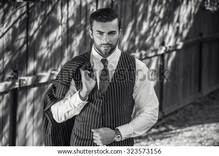Black-white portrait of young beautiful fashionable man against wooden fence In classic suit.