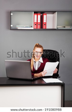 beautiful businesswoman sitting in office and reading paper. looking at camera