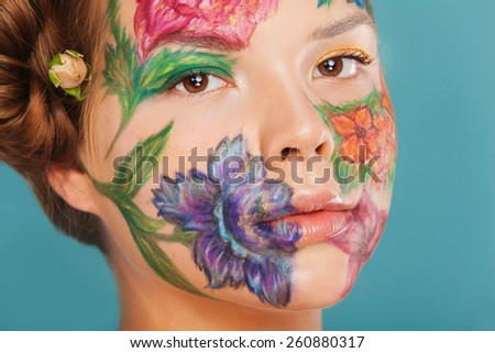 Close up portrait of woman model with hand drawing flowers on her face. Color face art woman. On blue background