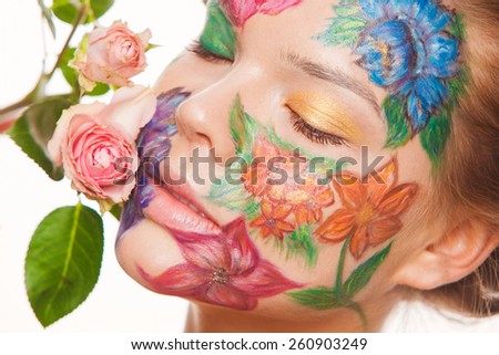 Spring portrait of woman model with hand drawing flowers on her face. Touching roses. Color face art woman. On blue background
