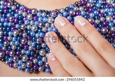 Young woman hands with natural french manicure on blue beads. care for sensuality woman nails