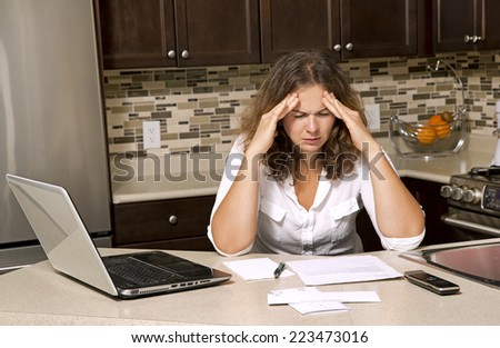 stressed woman looking at bills while sitting in the kitchen