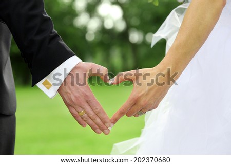 Bride and groom standing together and holding hands in shape of heart