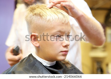 Barber cutting and modeling hair of young boy by electric trimmer