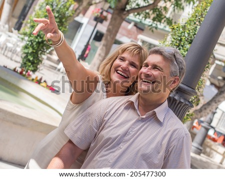 Romantic mature attractive couple pointing out something amusing to her husband as they stand close together in the summer sunshine sightseeing on their summer vacation to the tropics