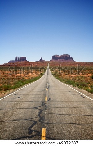 Looking down the center of an empty desert highway running through a valley with rock formations in the background. Vertical shot.