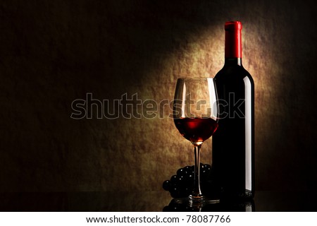 bottle with red wine and glass and grapes on a old stone