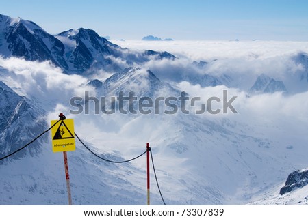 Yellow warning sign in front of beautiful mountain landscape. Sign warns about the risk of falling