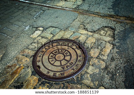 Manhole drain cover on rough old cobblestone and asphalt street at historic Brooklyn Navy Yard