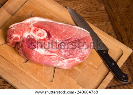 Raw cut of pork shoulder on cutting board with knife