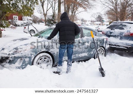 LONG ISLAND, NEW YORK - JANUARY 27,  2015:  Young man digging out and removing snow from cars after blizzard that hit the North East on Jan. 26 and 27, 2015.