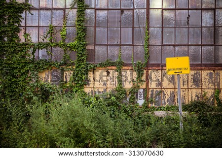 Grungy old industrial exterior with windows and overgrown vines and weeds