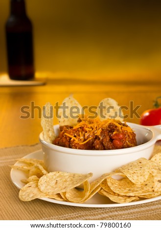 A bowl of chili con carne served with tortilla chips and a bottle of beer