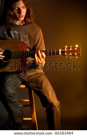 A young guy with long hair playing an acoustic guitar with golden light