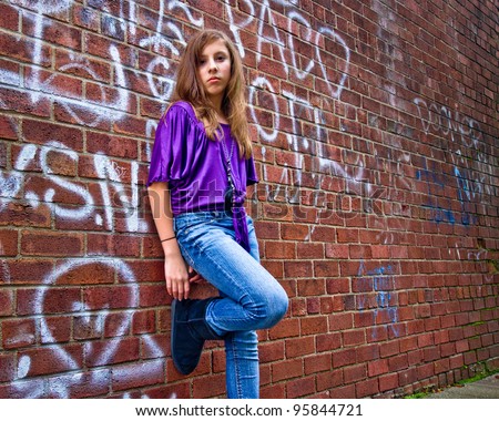 Cool teenage girl leaning casually against a graffiti covered urban wall