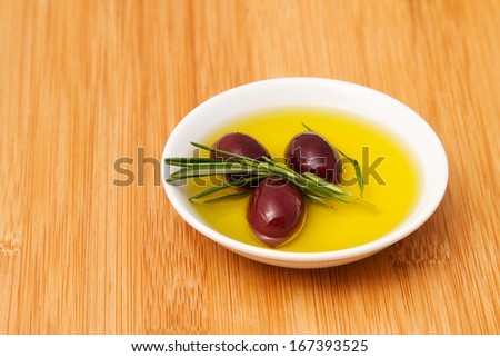 Bowl filled with olive oil and black pickled olives on wooden tabletop
