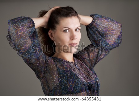 Portrait of young woman with hands behind neck on gray background