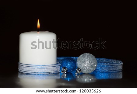 White Christmas candle with glittery baubles and a blue ribbon against dark background