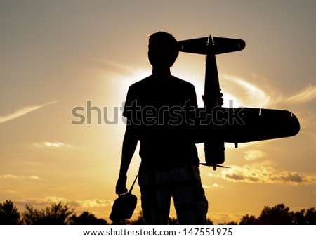Silhouette of a young man with a model rc airplane and a controller, against sunset sky