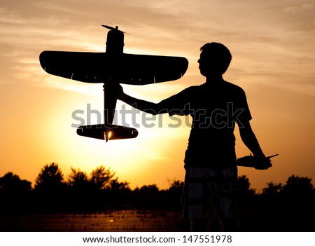Silhouette of a young man with a model rc airplane against sunset and clouds, with a sunburst