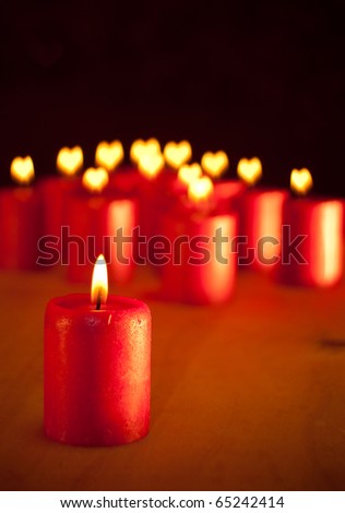 Red Christmas candle on table - with group of similar candles with hearts for flames on background