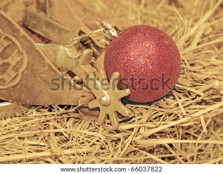 Cowboy Christmas - old spurs on hay with a red ball ornament in muted sepia tone