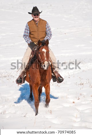 Man in cowboy hat riding a horse in snow towards the viewer