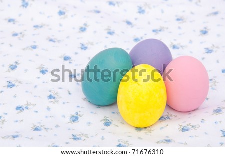 Pastel colored hand painted Easter eggs on a white cloth with delicate blue floral pattern