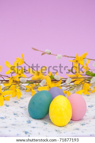 Bright Easter eggs on a floral patterned cloth with spring twigs, with copy space