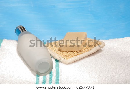Body lotion bottle, soap and an exfoliation pad on top of a white bath towel
