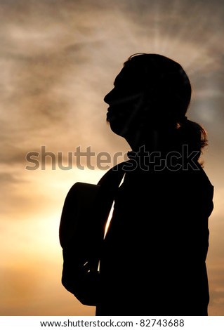 Silhouette of a young man with a ponytail gazing towards sky, holding his cowboy hat against his chest