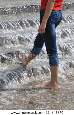Nice barefooted attractive magnetic legs in jeans of young svelte woman in micro-cascades of water at hot day