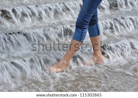 Nice barefooted legs in jeans of young  svelte woman are cooling in microcascades of water at hot day