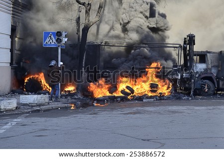 KIEV UKRAINE-FEBRUARY 18, 2014: Fire protecting by defend oneself protesters of  armed forces attack at first day of mass shooting in Kyiv at Euromaydan time. Protester in helmet near ablaze cars.