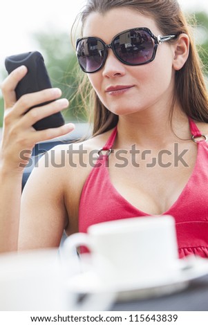 A beautiful young woman texting on her mobile cell phone while drinking coffee in a cafe